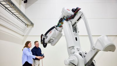 Zwei Ingenieure programmieren einen großen, weißen ABB-Industrieroboterarm in einer Laborumgebung.