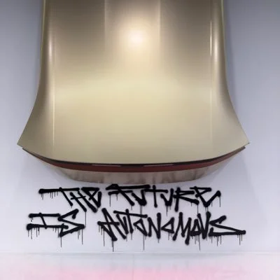 Elon Musks X-Avatar zeigt eine Motorhaube mit Graffiti-Aufschrift 'The Future is Autonomous'