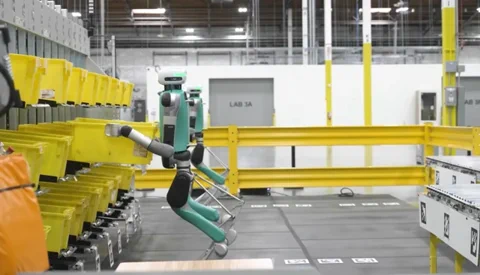 Die vorherige Generation des Digit-Roboters von Agility mit seinen ikonischen, nach hinten gebogenen Beinen beim Bewegen von Behältern in einem Lagerhaus.