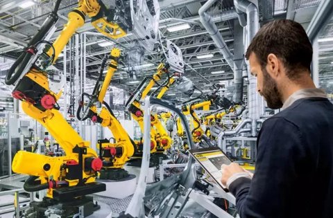Ein Ingenieur verwaltet mit einem Tablet eine Fabrikhalle voller gelber FANUC-Roboterarme.