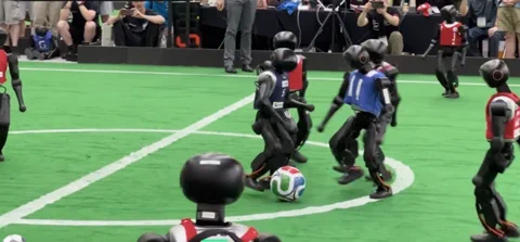 Zwei Teams humanoider Roboter beim ersten 11-gegen-11-Fußballspiel auf dem RoboCup 2026 auf einem grünen Spielfeld.